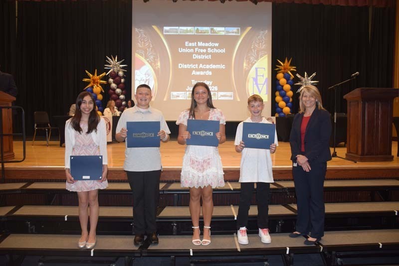 Photo of students standing on risers while holding certificates, medals and awards for their excellence in academics, athletics, clubs and community service.