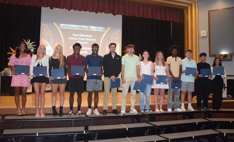 Photo of students standing on risers while holding certificates, medals and awards for their excellence in academics, athletics, clubs and community service.