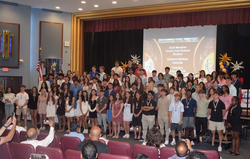 Photo of students standing on risers while holding certificates, medals and awards for their excellence in academics, athletics, clubs and community service.
