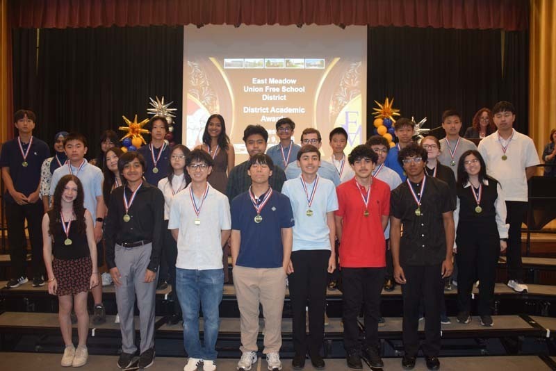 Photo of students standing on risers while holding certificates, medals and awards for their excellence in academics, athletics, clubs and community service.