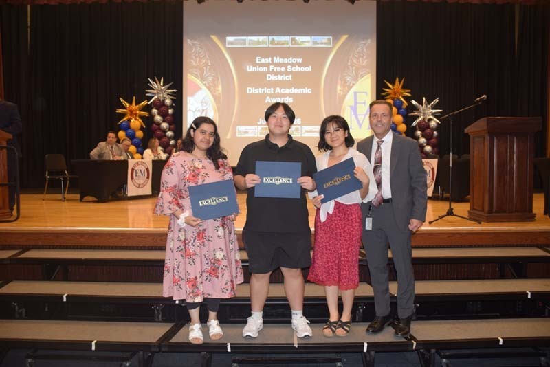 Photo of students standing on risers while holding certificates, medals and awards for their excellence in academics, athletics, clubs and community service.