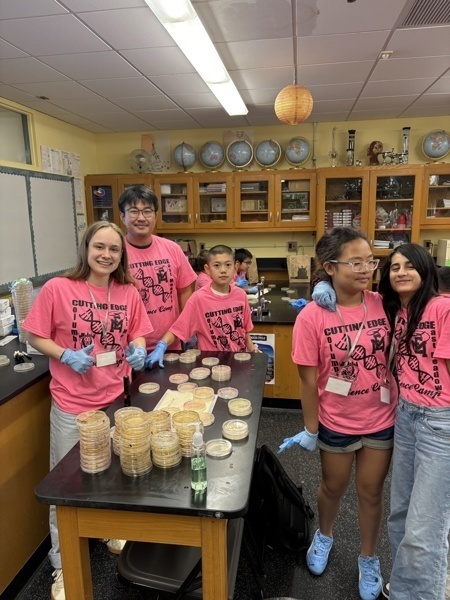 Photo of STEM students wearing pink t-shirts in science lab while working on a group experiment.
