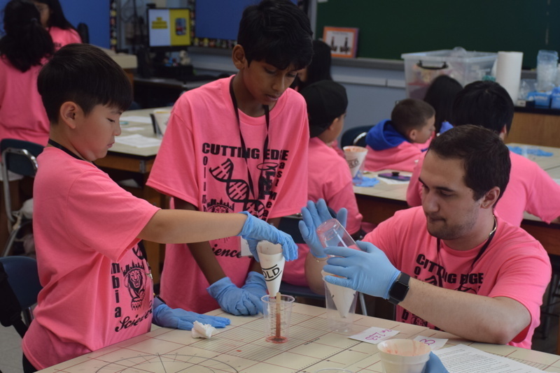 Photo of STEM students wearing pink t-shirts in science lab while working on a group experiment.