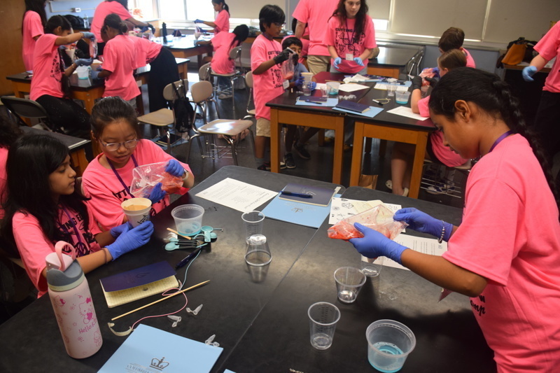 Photo of STEM students wearing pink t-shirts in science lab while working on a group experiment.