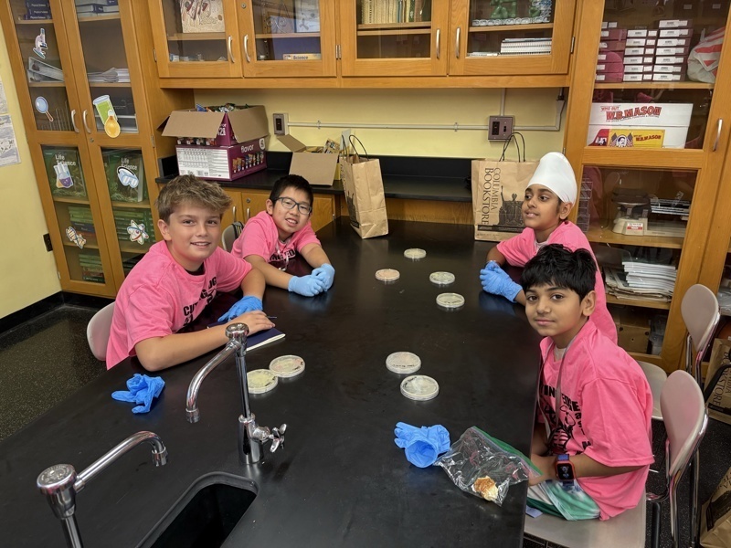 Photo of STEM students wearing pink t-shirts in science lab while working on a group experiment.