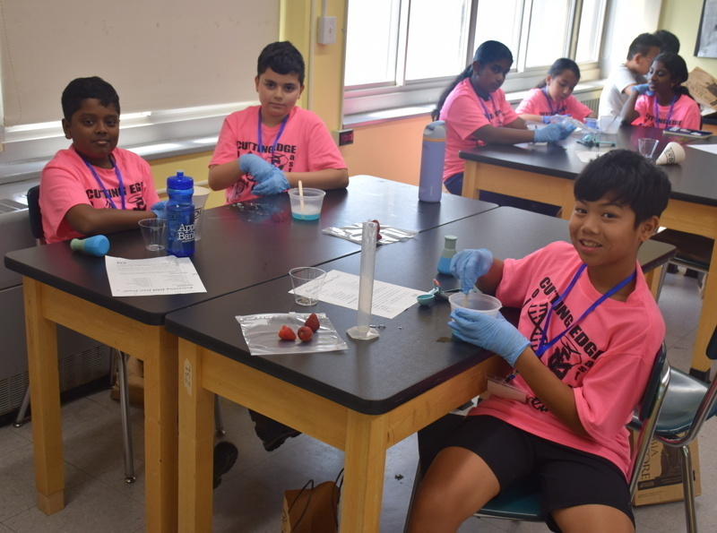 Photo of STEM students wearing pink t-shirts in science lab while working on a group experiment.