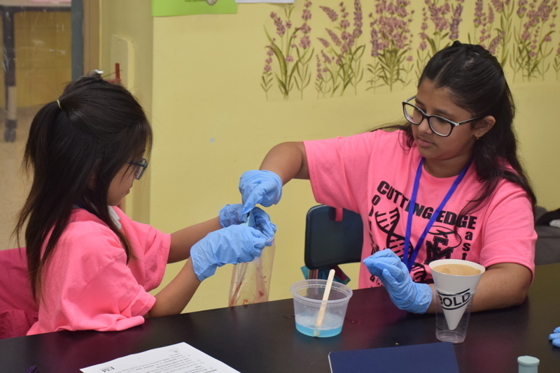 Photo of STEM students wearing pink t-shirts in science lab while working on a group experiment.