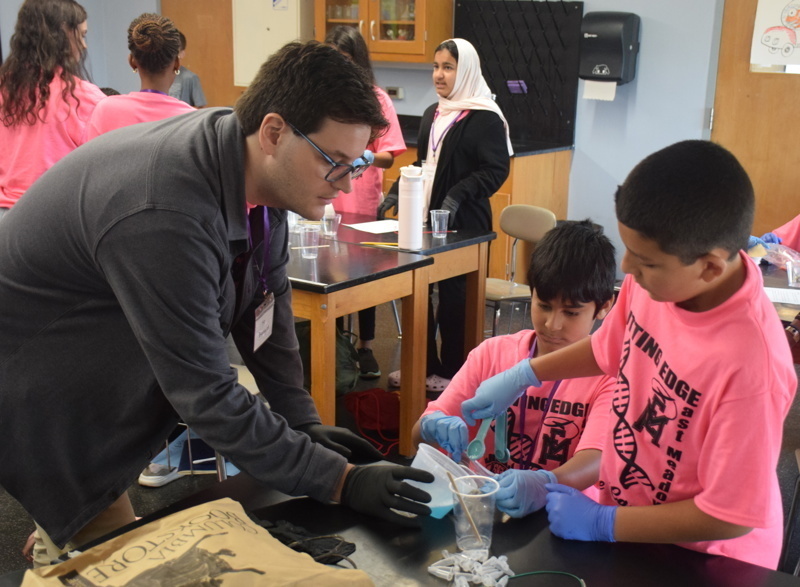 Photo of STEM students wearing pink t-shirts in science lab while working on a group experiment.
