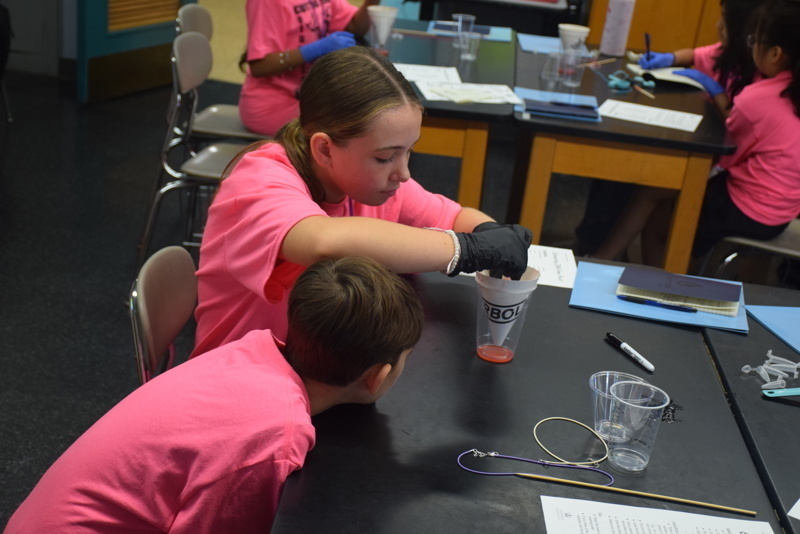 Photo of STEM students wearing pink t-shirts in science lab while working on a group experiment.
