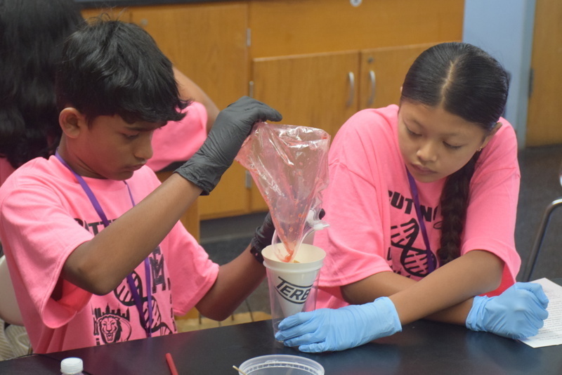 Photo of STEM students wearing pink t-shirts in science lab while working on a group experiment.