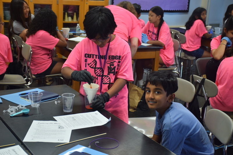 Photo of STEM students wearing pink t-shirts in science lab while working on a group experiment.