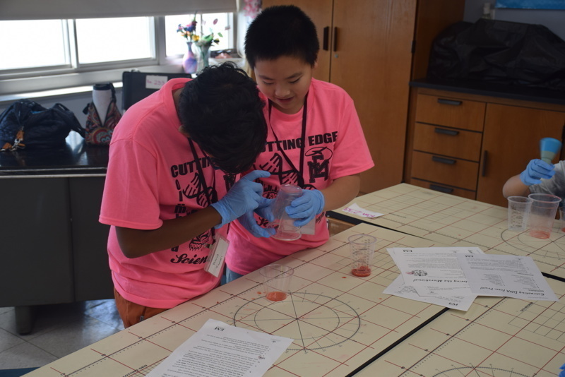 Photo of STEM students wearing pink t-shirts in science lab while working on a group experiment.