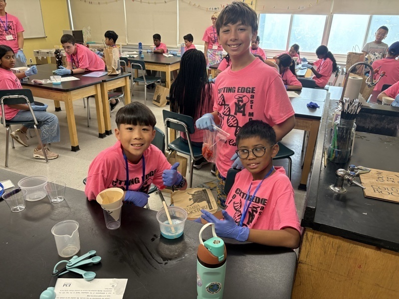 Photo of STEM students wearing pink t-shirts in science lab while working on a group experiment.