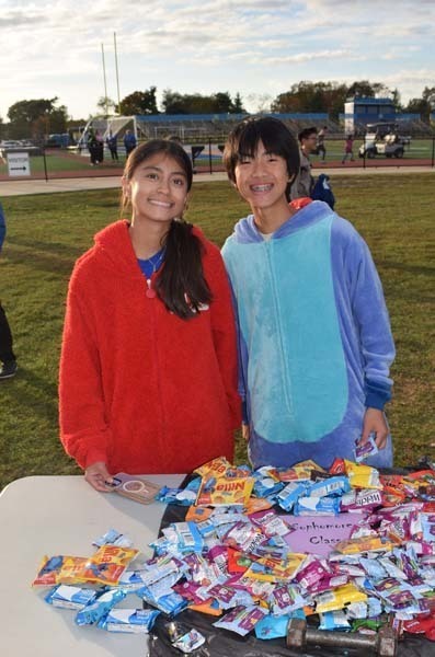 Photo of students dressed up in Halloween costumes outside in front of their tables with candy.
