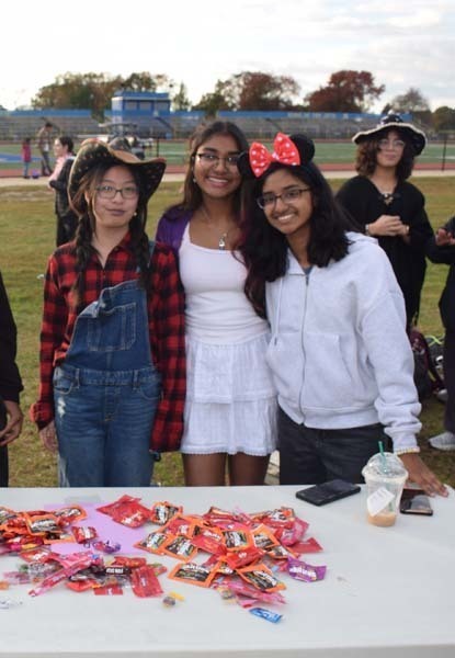 Photo of students dressed up in Halloween costumes outside in front of their tables with candy.