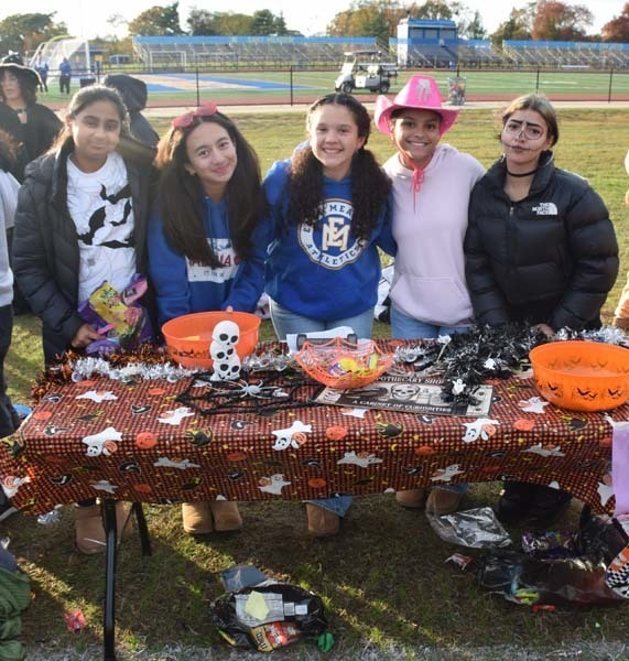 Photo of students dressed up in Halloween costumes outside in front of their tables with candy.