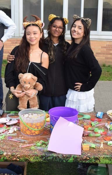 Photo of students dressed up in Halloween costumes outside in front of their tables with candy.
