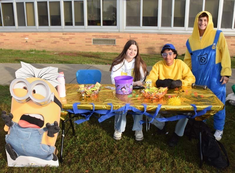 Photo of students dressed up in Halloween costumes outside in front of their tables with candy.