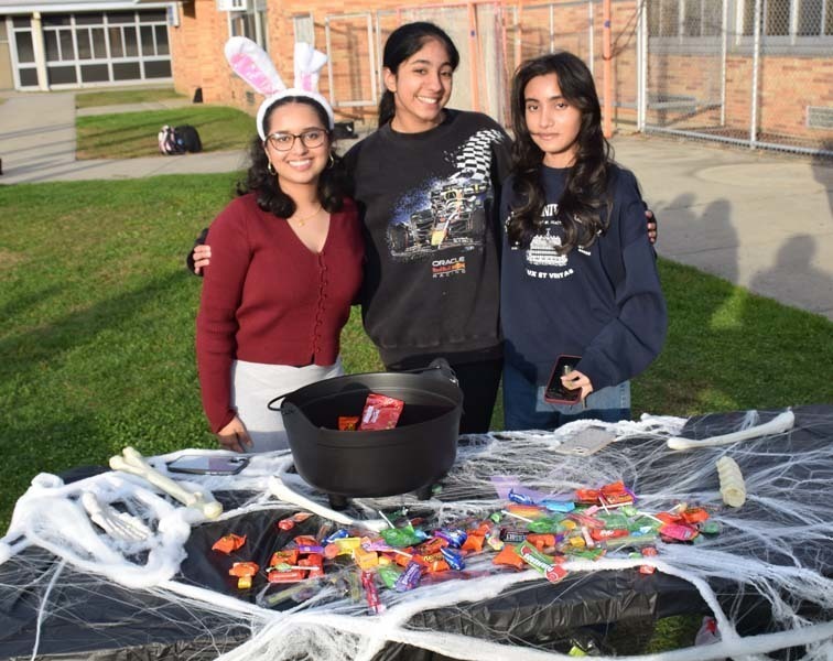 Photo of students dressed up in Halloween costumes outside in front of their tables with candy.