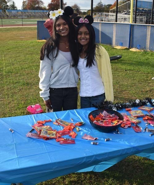Photo of students dressed up in Halloween costumes outside in front of their tables with candy.