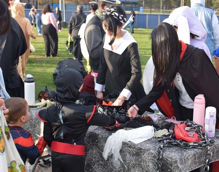 Photo of students dressed up in Halloween costumes outside in front of their tables with candy.