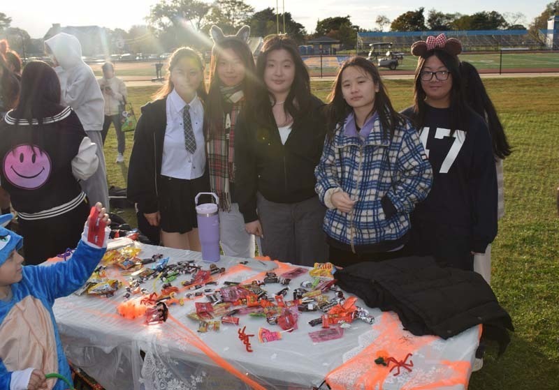 Photo of students dressed up in Halloween costumes outside in front of their tables with candy.