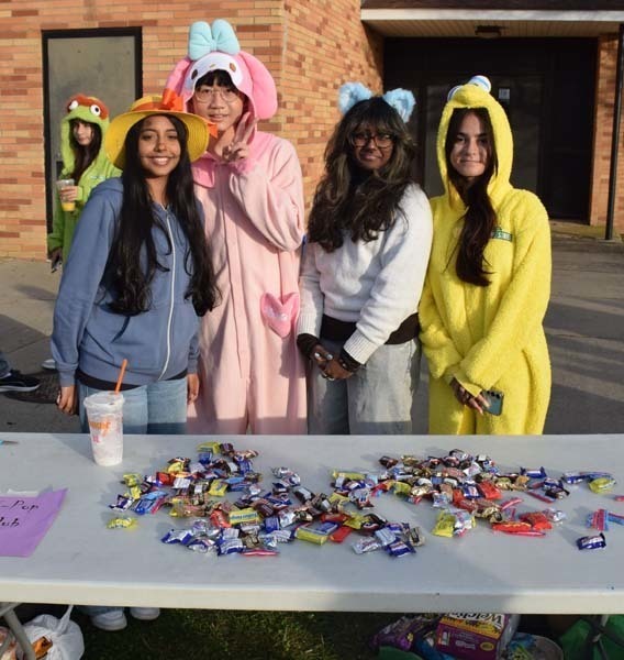 Photo of students dressed up in Halloween costumes outside in front of their tables with candy.