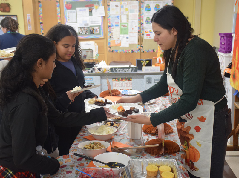 Seven kids sit around a festive table with autumn-themed decorations and paper pumpkins. They smile and show thumbs-up, conveying a joyful atmosphere.