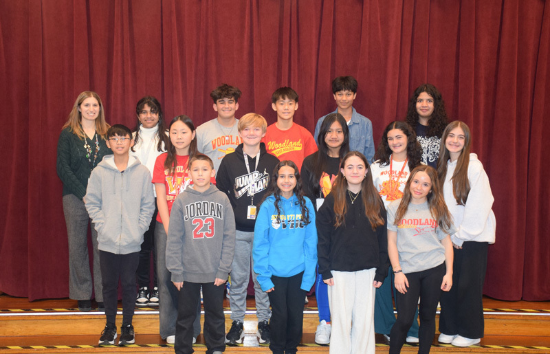 A diverse group of teenagers and adults stand on risers against a purple curtain backdrop, smiling warmly, conveying a sense of camaraderie and community.