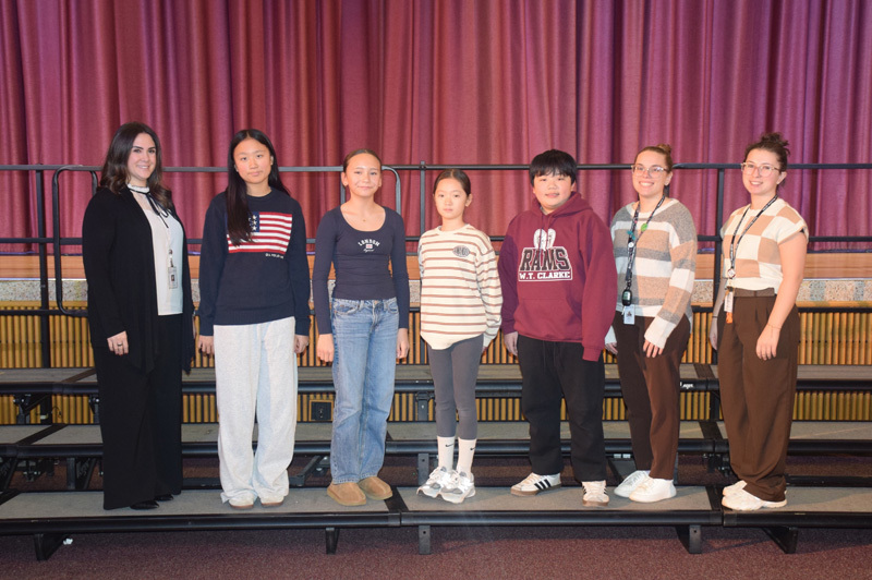 A diverse group of teenagers and adults stand on risers against a purple curtain backdrop, smiling warmly, conveying a sense of camaraderie and community.