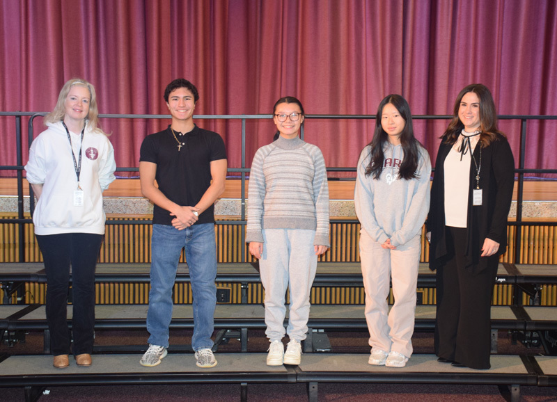A diverse group of teenagers and adults stand on risers against a purple curtain backdrop, smiling warmly, conveying a sense of camaraderie and community.