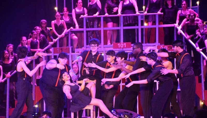 Photo of students wearing black and red clothing while performing on stage.