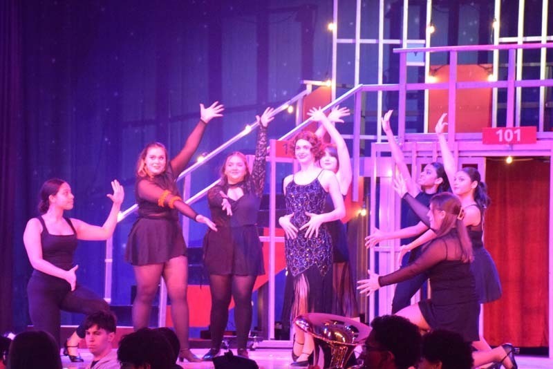 Photo of female students performing on stage under red and pink lights.