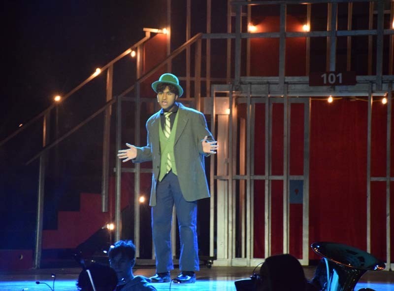 Photo of student wearing green suit and hat performing a musical on stage.