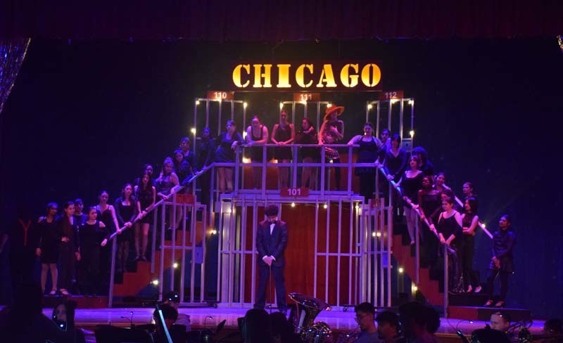 Photo of students performing under dark blue lighting on stage with a sign at the top that reads Chicago.