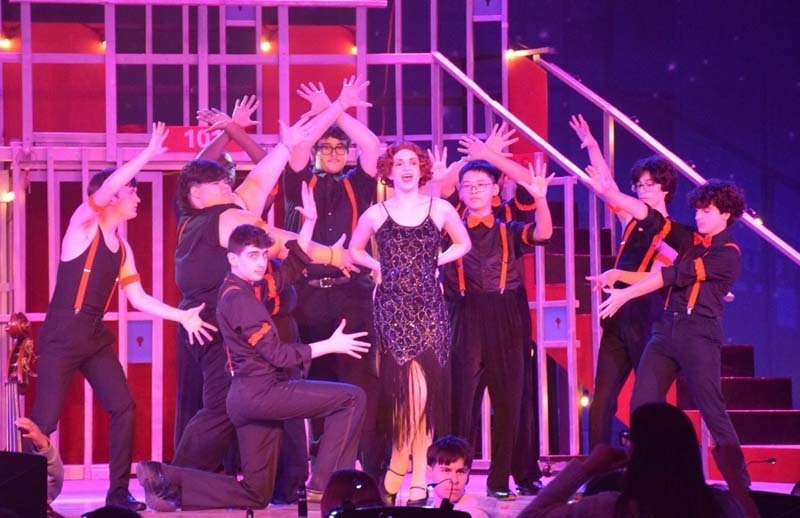 Photo of students performing on stage under red and pink lights.