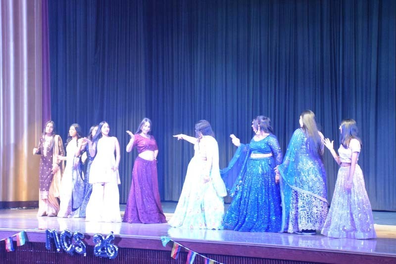 Photo of students wearing traditional, colorful dresses from their home country while dancing.