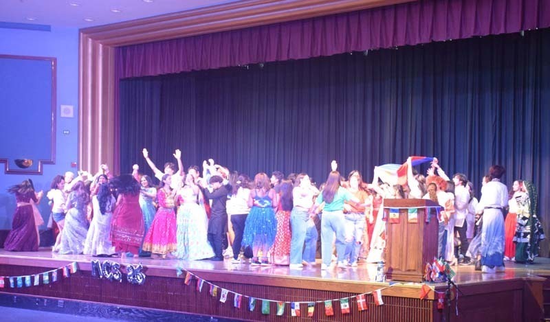 Photo of students wearing traditional, colorful dresses from their home country while dancing.
