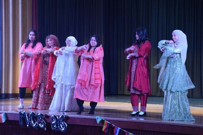 Photo of students wearing traditional, colorful dresses from their home country while dancing.