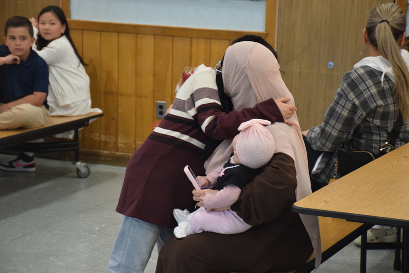 Photo of mother hugging her son while holding her baby daughter in school cafeteria.