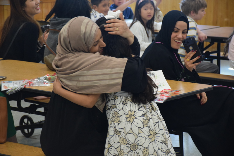 Photo of mother hugging her son while holding her baby daughter in school cafeteria.