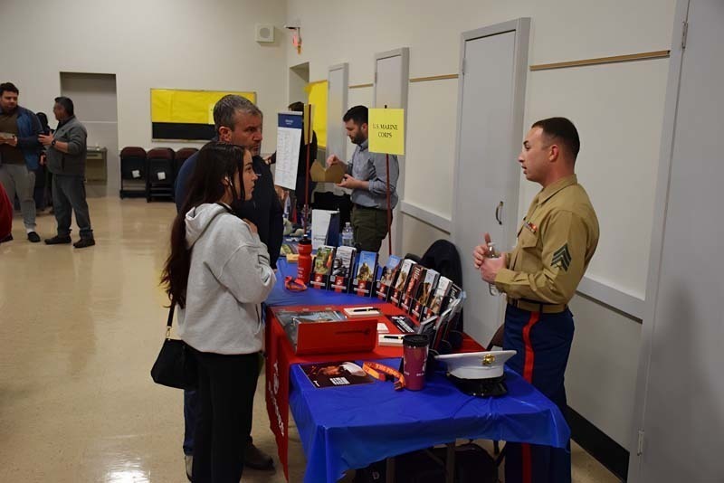 People talking at a college fair booth in the gym