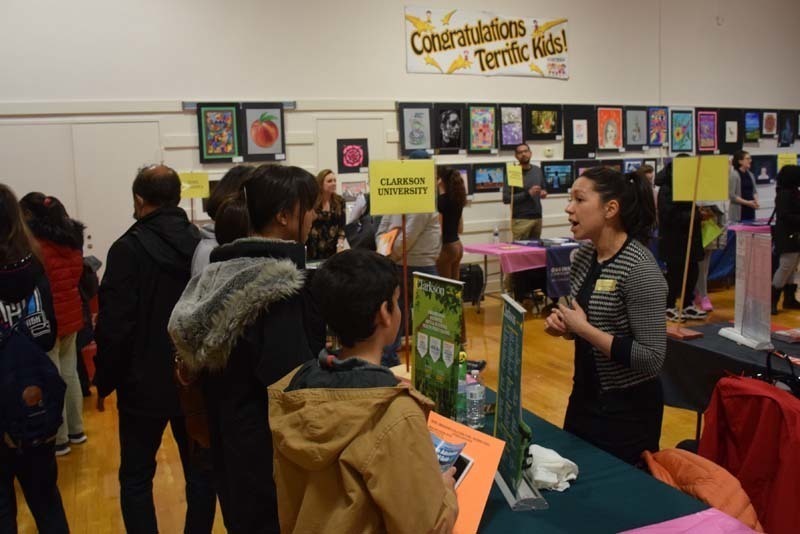 People talking at a college fair booth in the gym