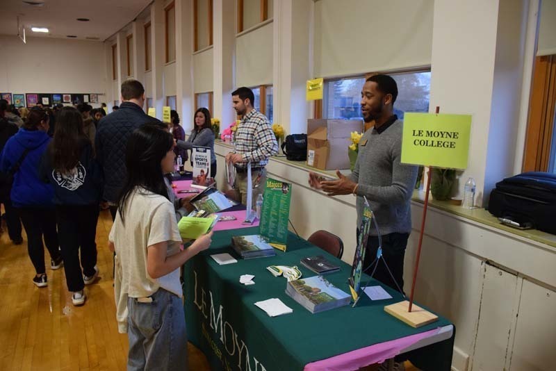 People talking at a college fair booth in the gym