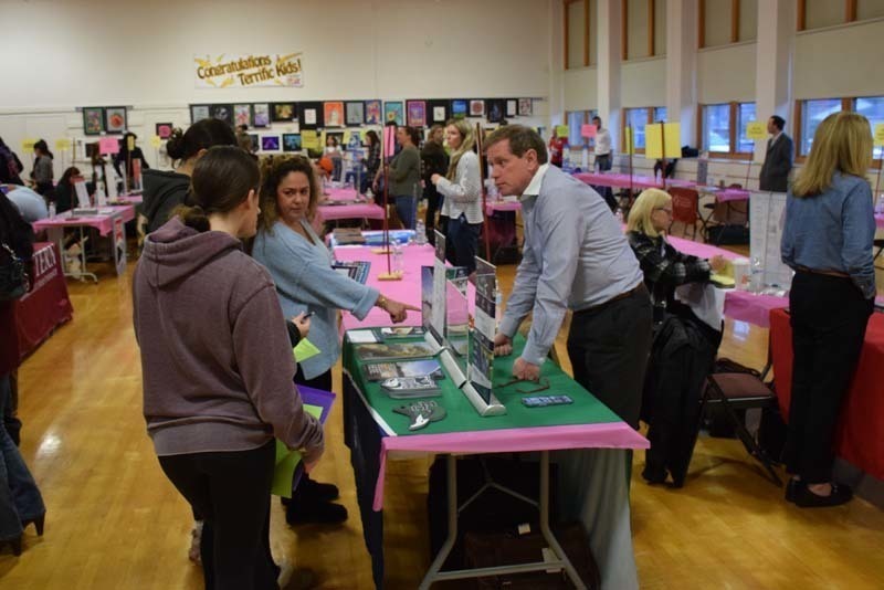 People talking at a college fair booth in the gym