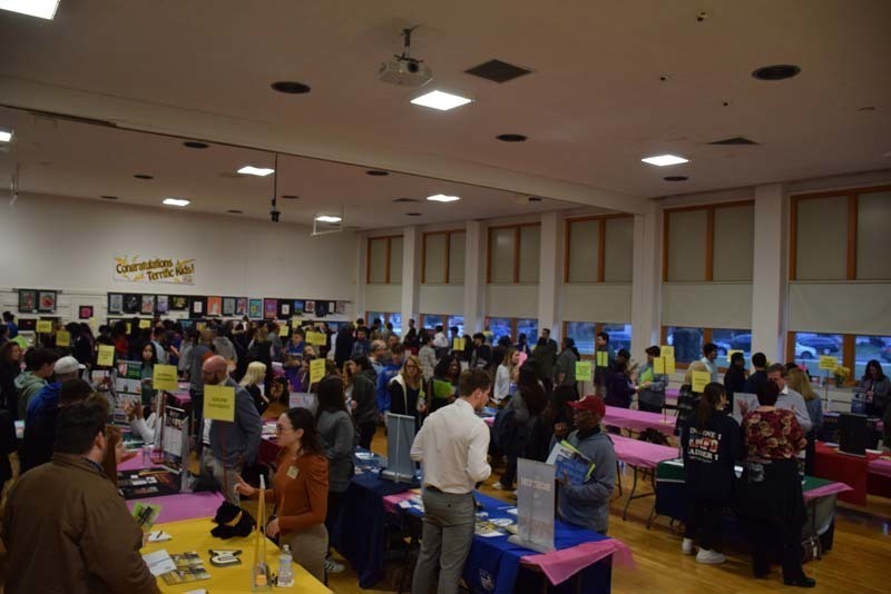 People talking at a college fair booth in the gym