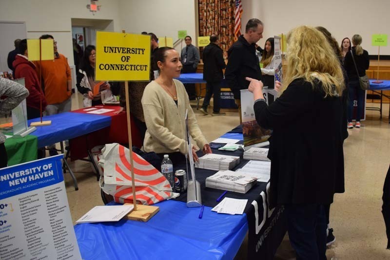 People talking at a college fair booth in the gym