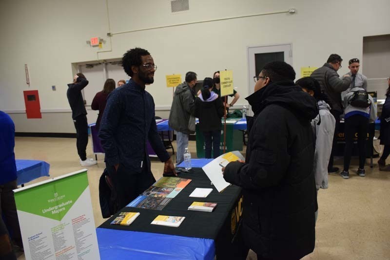 People talking at a college fair booth in the gym