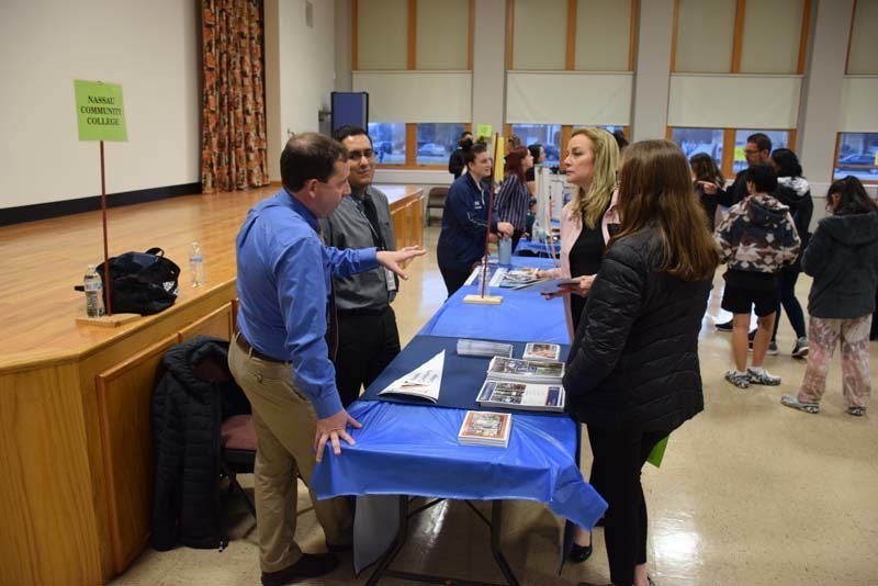 People talking at a college fair booth in the gym