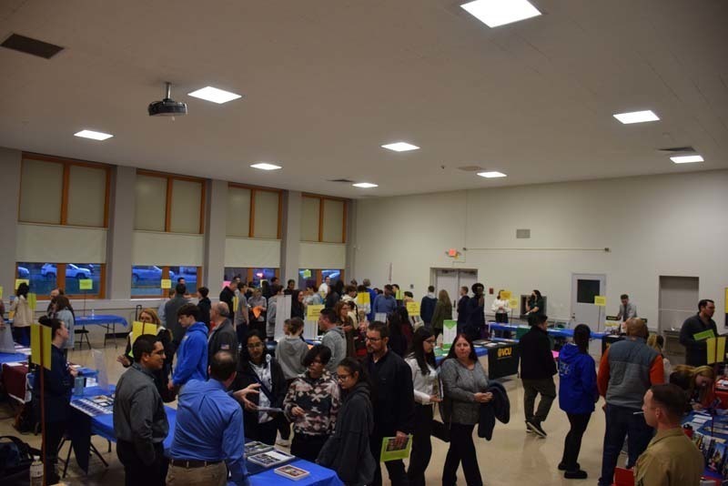 People talking at a college fair booth in the gym
